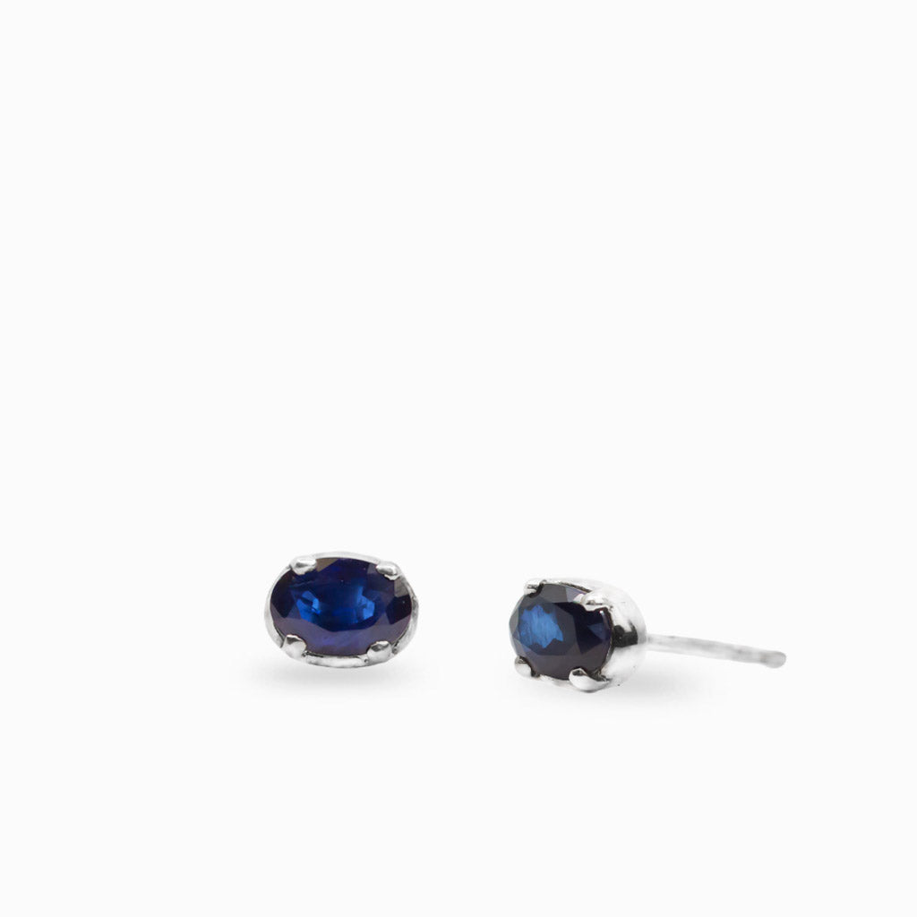 Oval faceted blue Sapphire stud earrings in polished 925 sterling silver prong settings with rich deep-blue coloring.