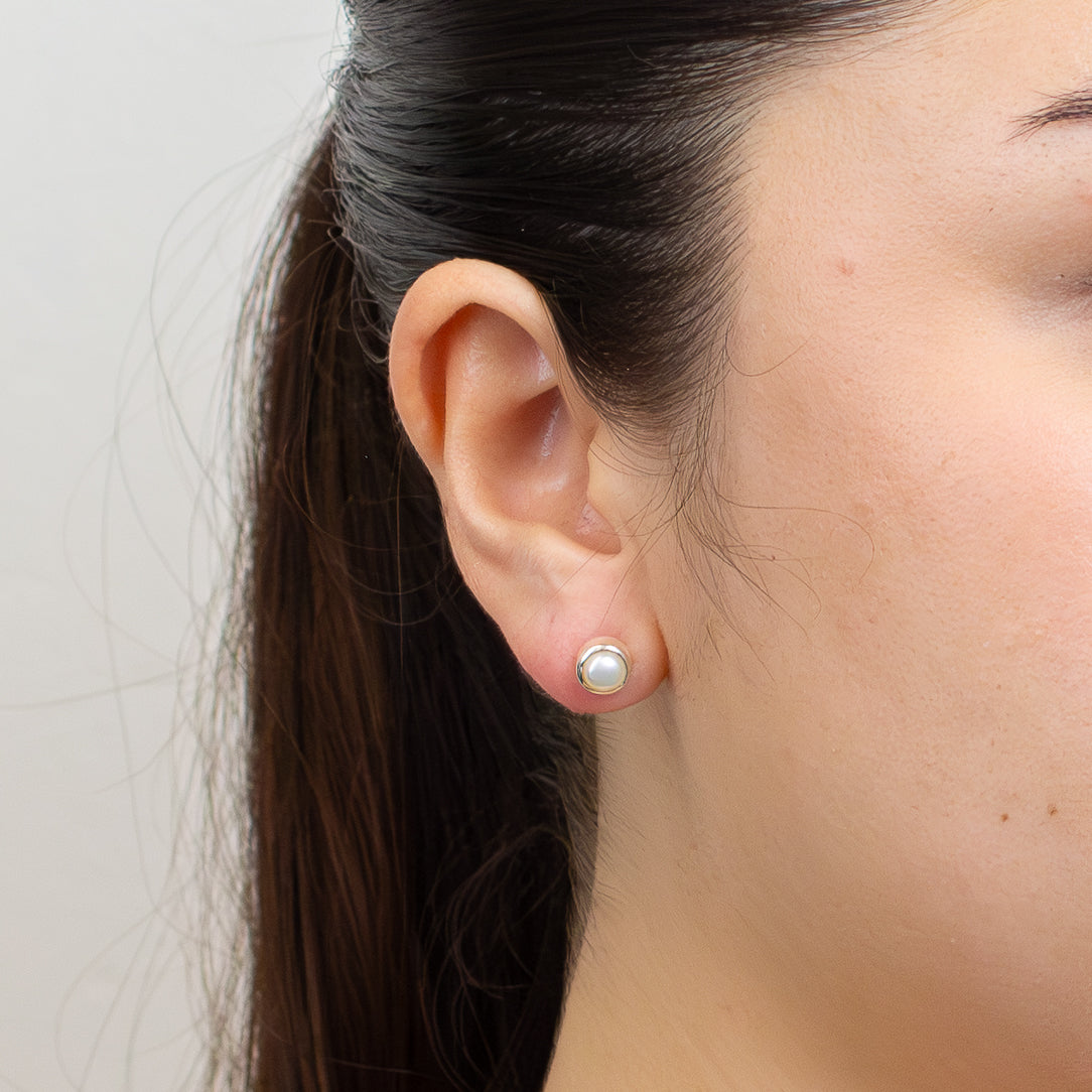 Close-up of an ear wearing a pearl stud earring with a plain background