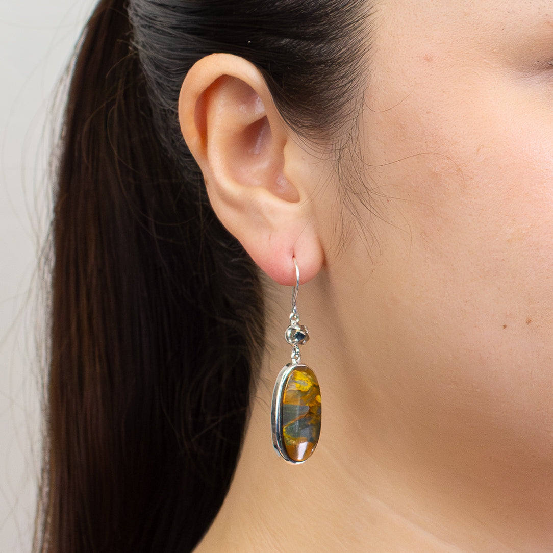 Oval Pietersite and Pyrite cabochon earrings set in sterling silver, featuring stormy blue, gold, and charcoal gemstone patterns ON MODEL