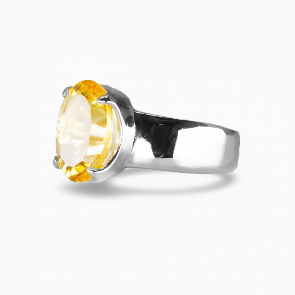 Faceted oval yellow Citrine ring set in a sterling silver prong setting with a wide silver band, photographed on a white background