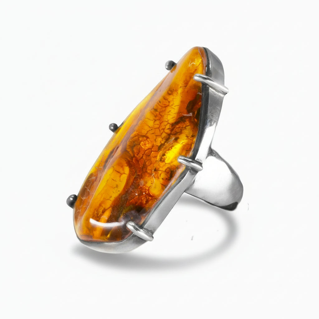 Organic-shaped Amber ring with warm golden-orange tones and natural inclusions set in a sterling silver prong setting on a white background. | MADE IN EARTH USA