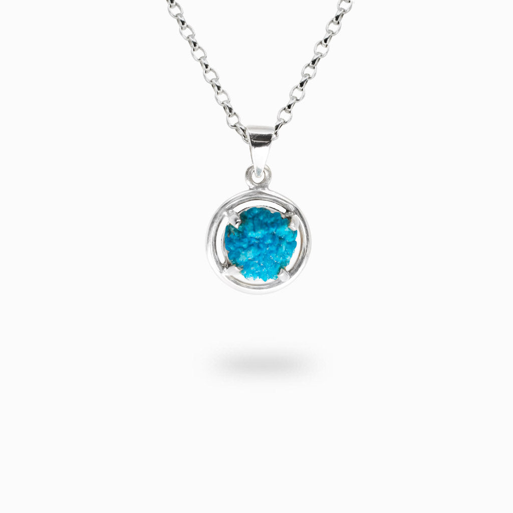 Vivid blue raw Cavansite crystal held in a sterling silver claw setting within a circular halo pendant.