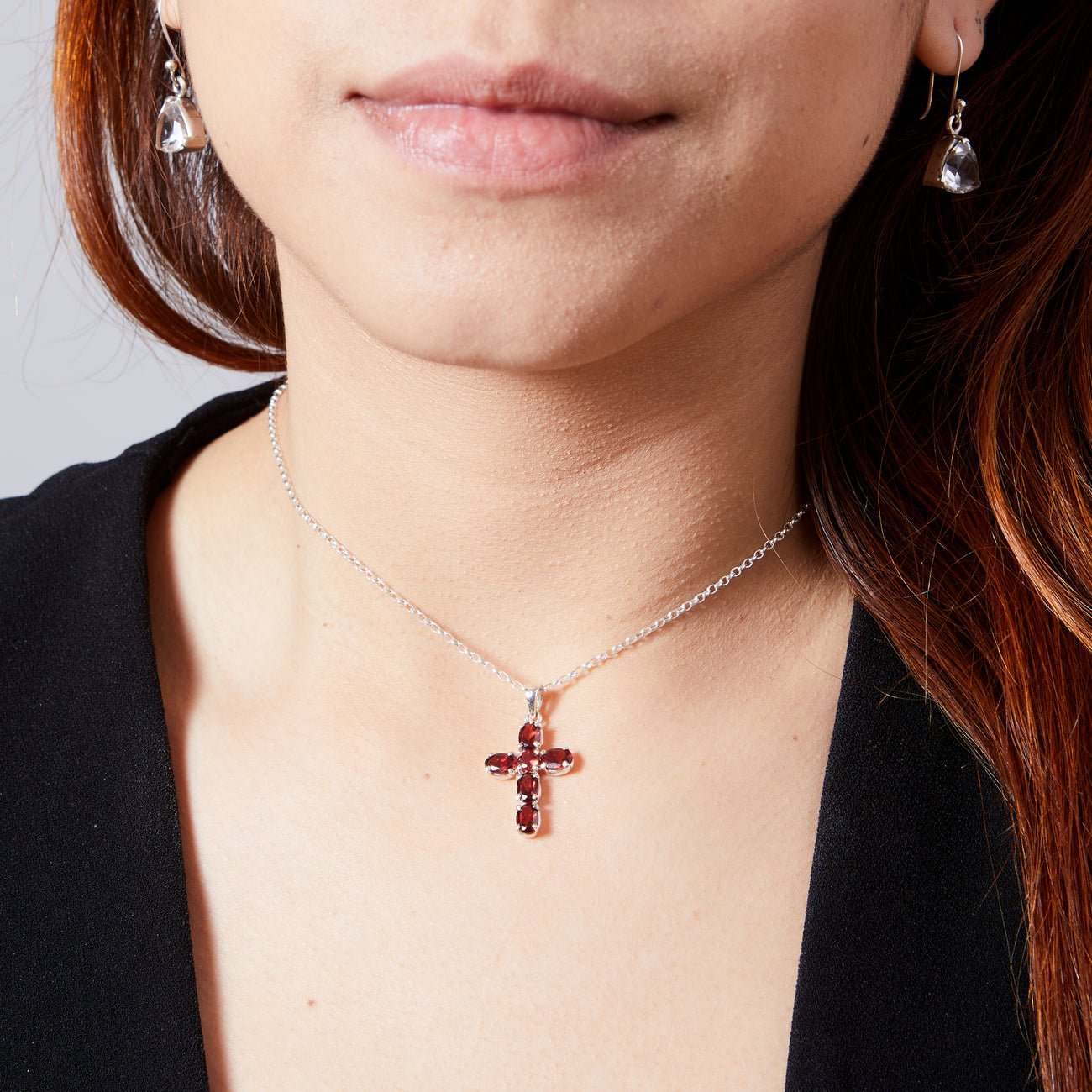 Close-up of a person wearing a silver necklace with a red GARNET gemstone cross pendant.