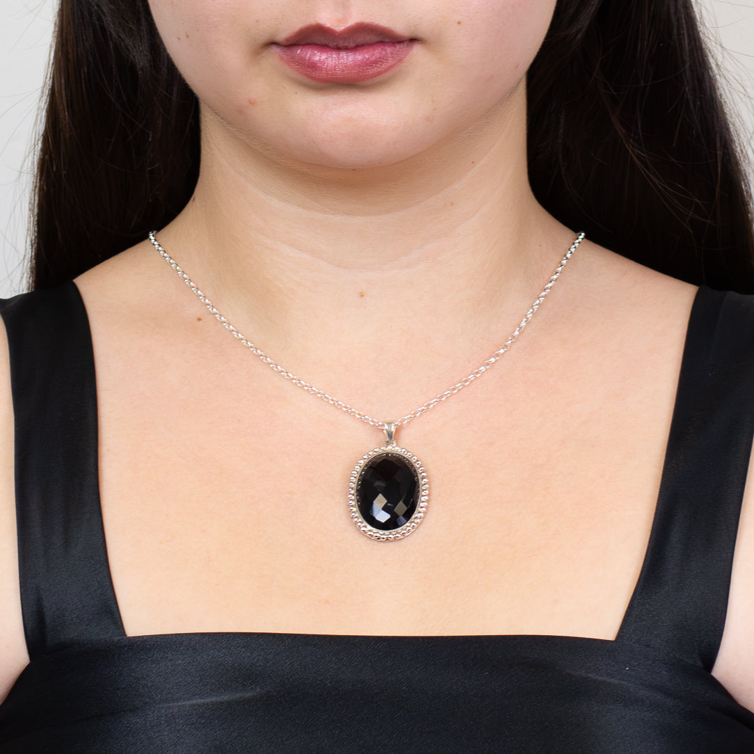 Faceted oval black onyx pendant set in sterling silver on chain on model