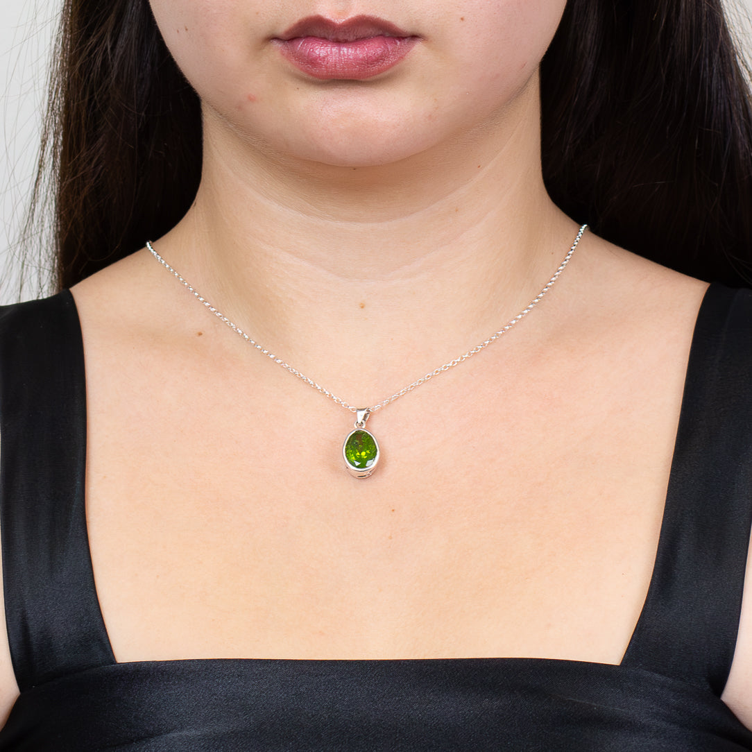 Faceted oval peridot gemstone pendant necklace set in sterling silver bezel on chain on model.