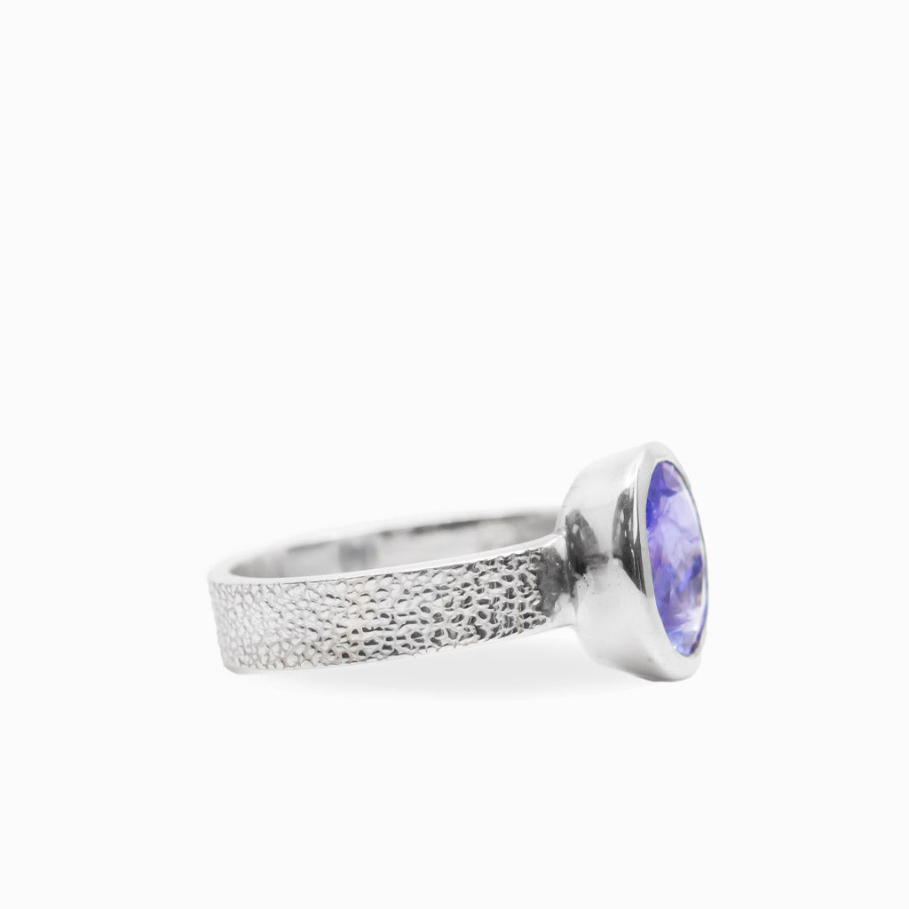 Oval faceted violet-blue Tanzanite ring in polished 925 sterling silver bezel setting with a broad textured silver band.