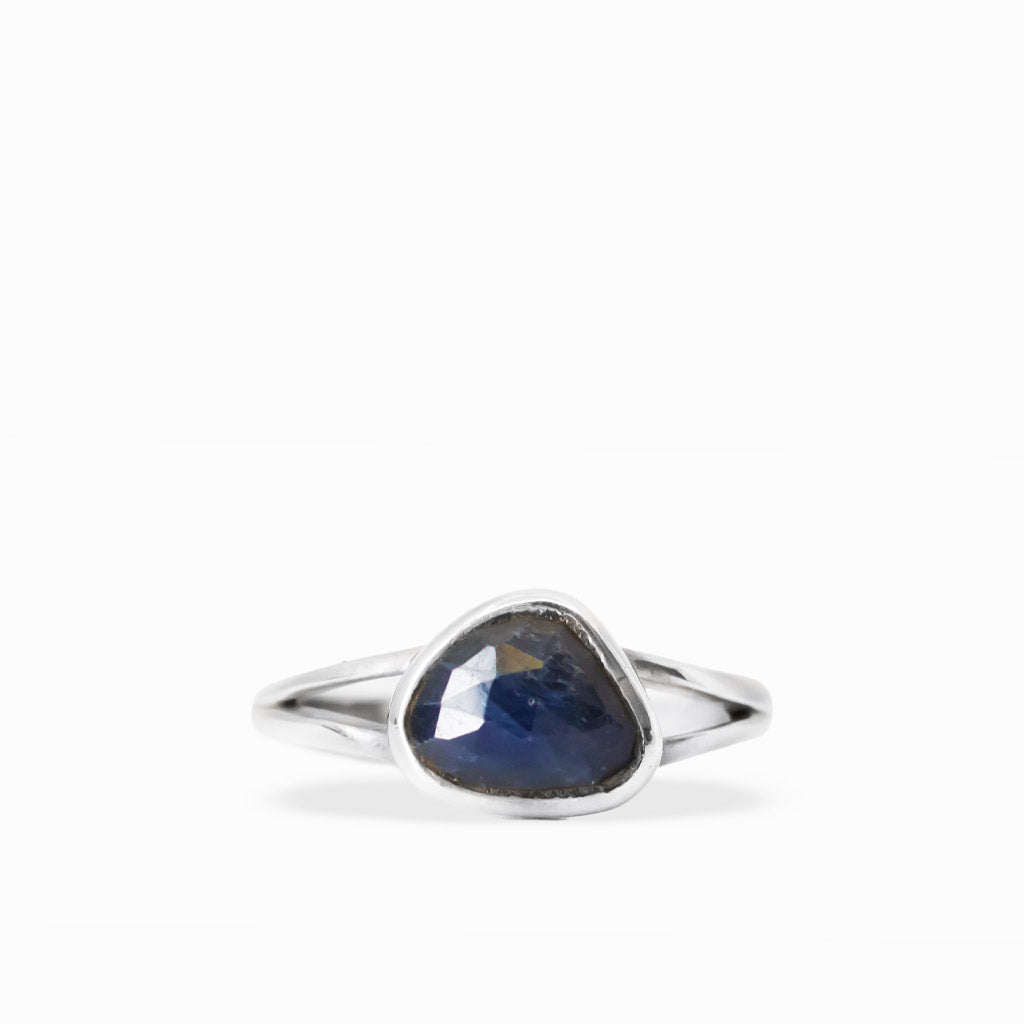 Deep midnight-blue freeform triangular Sapphire ring with faceted gemstone surface, sterling silver bezel setting, and split band.