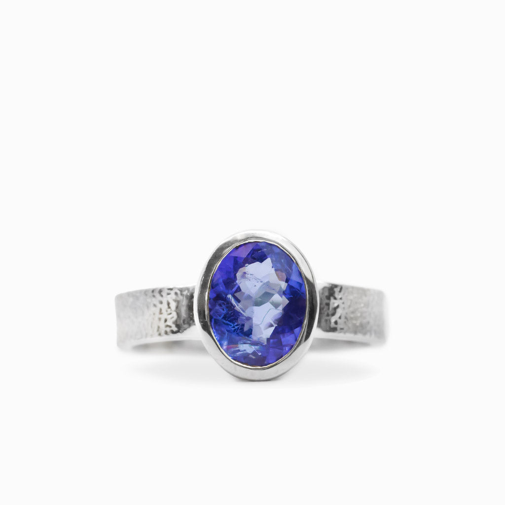 Oval faceted violet-blue Tanzanite ring in polished 925 sterling silver bezel setting with a broad textured silver band.