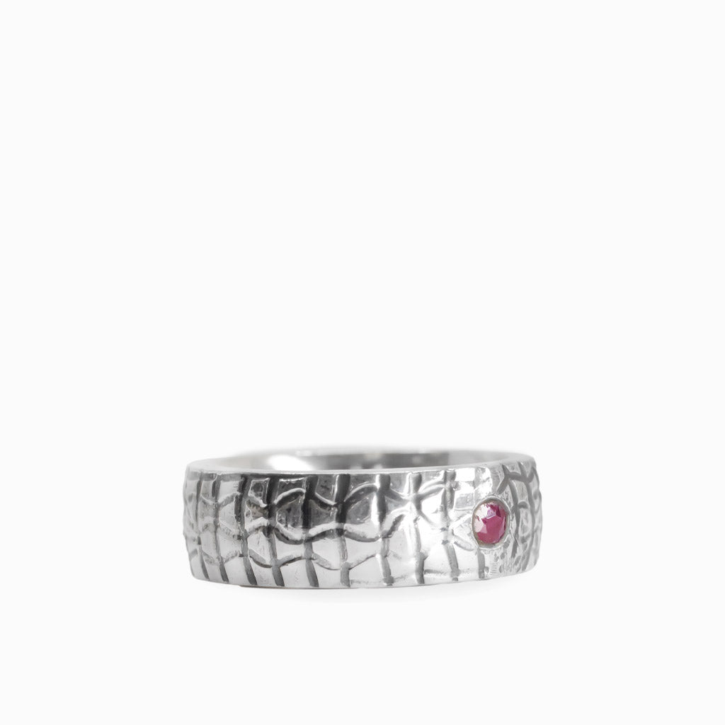 Small round red Ruby gemstone set into a wide textured 925 sterling silver band ring.