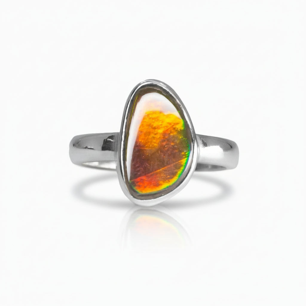Freeform Ammolite ring in sterling silver with vivid red, gold, and green iridescent flashes from a fossilized ammonite shell on a white background. | MADE IN EARTH