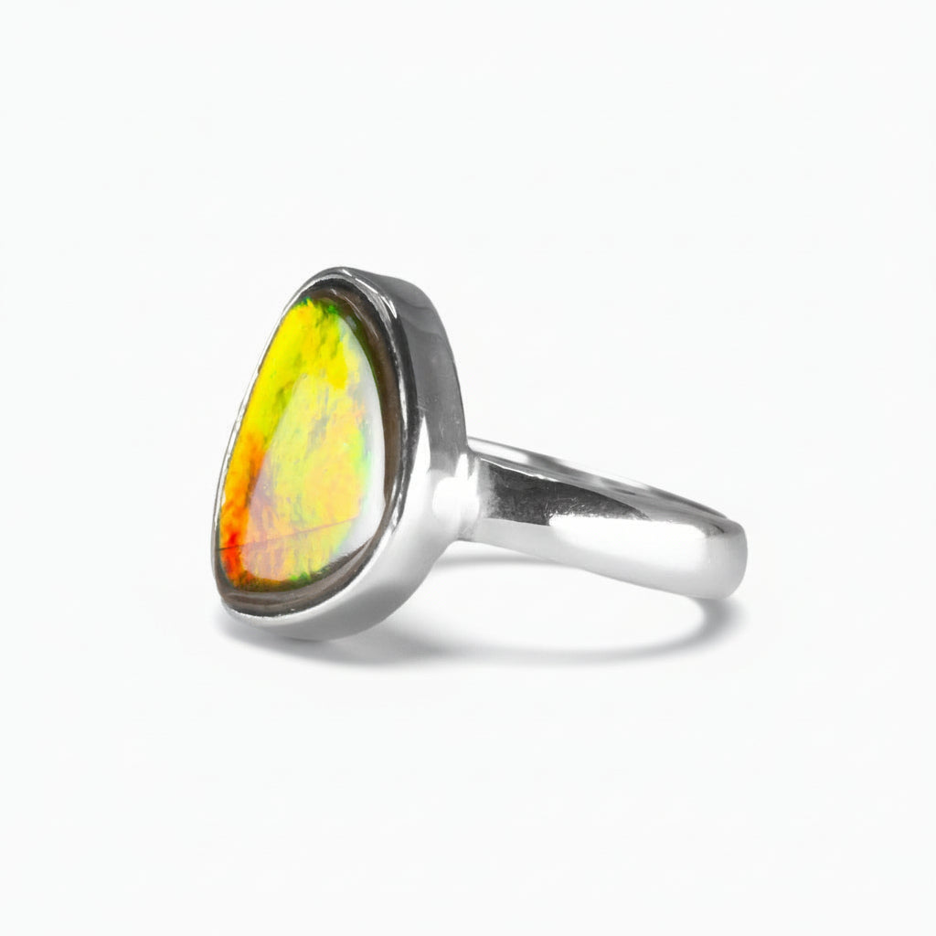 Freeform Ammolite ring in sterling silver with vivid red, gold, and green iridescent flashes from a fossilized ammonite shell on a white background. | MADE IN EARTH