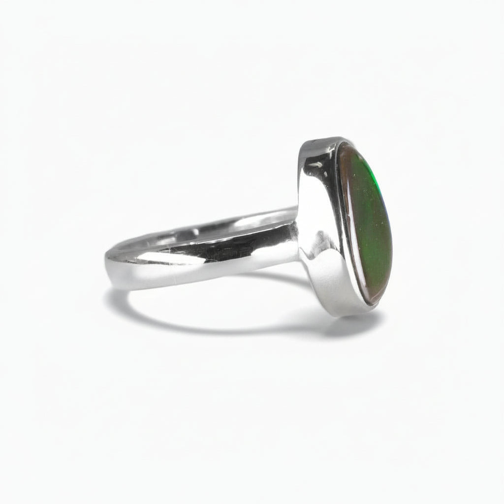Freeform Ammolite ring in sterling silver with vivid red, gold, and green iridescent flashes from a fossilized ammonite shell on a white background. | MADE IN EARTH