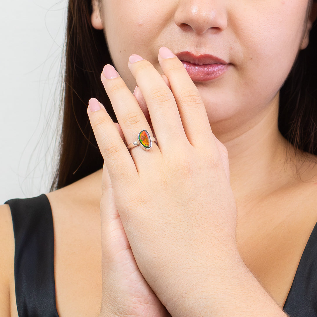 model wearing Freeform Ammolite ring in sterling silver with vivid red, gold, and green iridescent flashes from a fossilized ammonite shell on a white background. | MADE IN EARTH