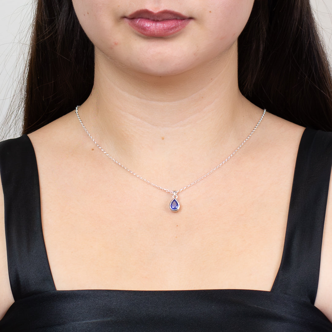 Faceted tear-shaped tanzanite gemstone pendant set in sterling silver bezel on model.
