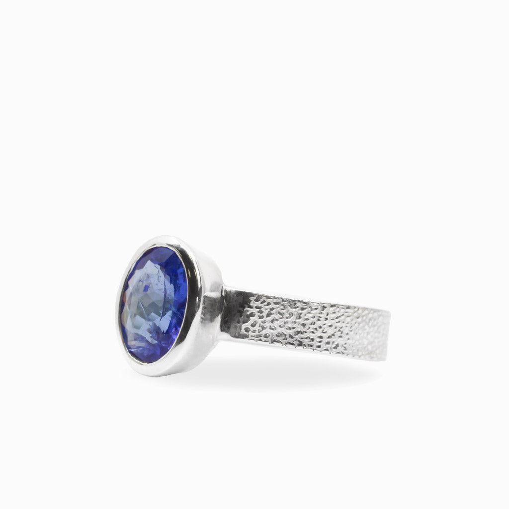 Oval faceted violet-blue Tanzanite ring in polished 925 sterling silver bezel setting with a broad textured silver band.