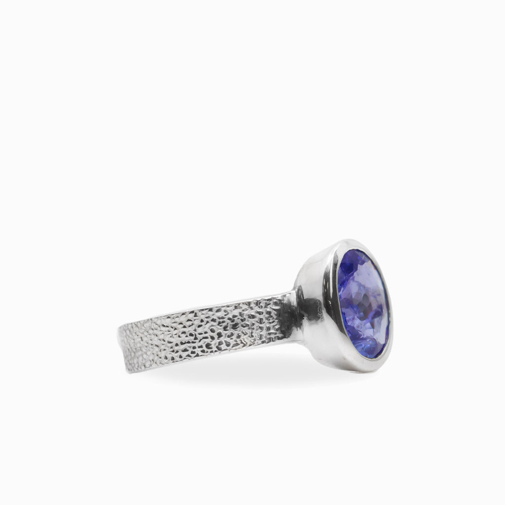Oval faceted violet-blue Tanzanite ring in polished 925 sterling silver bezel setting with a broad textured silver band.
