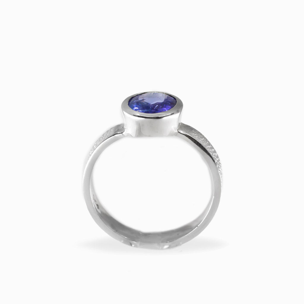 Oval faceted violet-blue Tanzanite ring in polished 925 sterling silver bezel setting with a broad textured silver band.